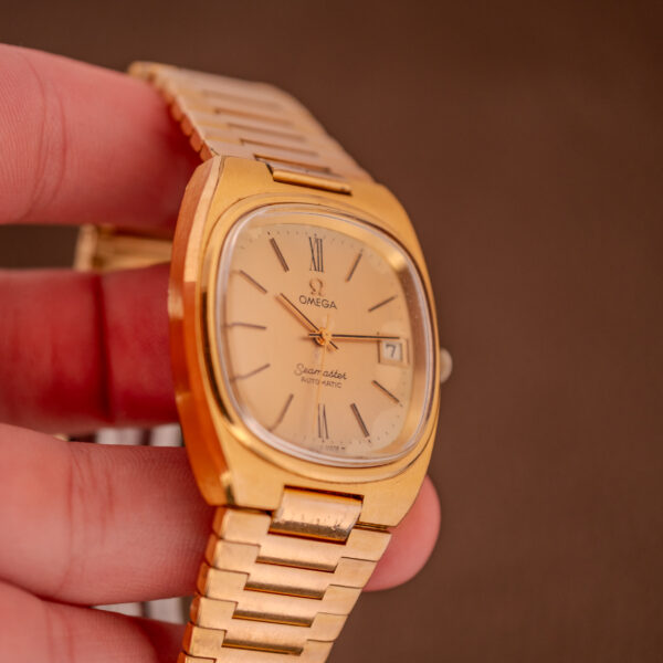 A hand holding an Omega Seamaster Automatic Date "TV Case" Ref. 166.0207 Cal. 1010, featuring a square face and metal band.