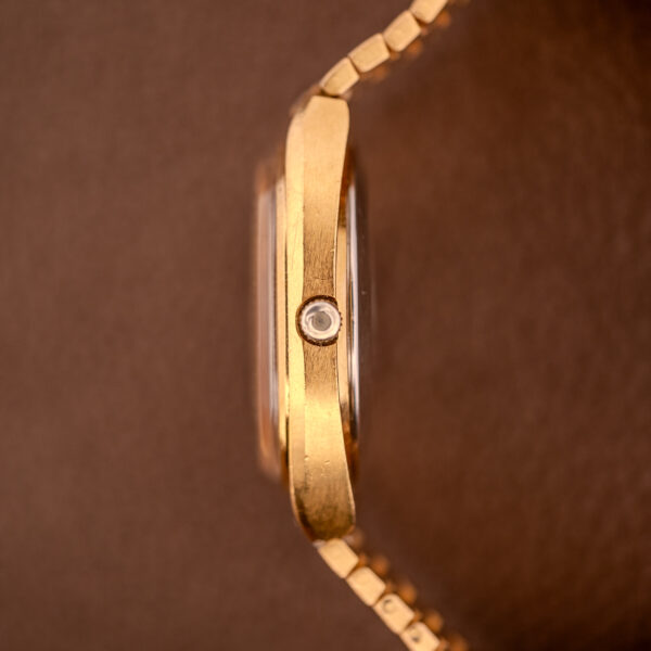 A close-up side view of an Omega Seamaster Automatic Date "TV Case" Ref. 166.0207 Cal. 1010 gold wristwatch, set against a brown background.