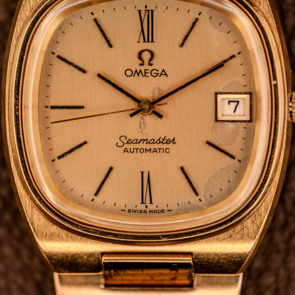 Close-up of an Omega Seamaster Automatic Date "TV Case" Ref. 166.0207 Cal. 1010, showcasing its gold-toned dial, hands, and distinctive automatic date window.