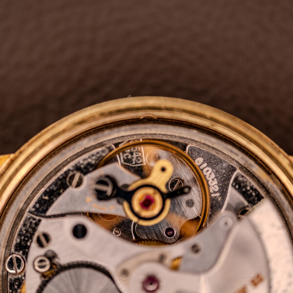 Close-up of a Zenith Automatic Date Cal. 2542 25 Jewels Sunburst Dial watch’s mechanical movement, showing gears and intricate components against a brown background.