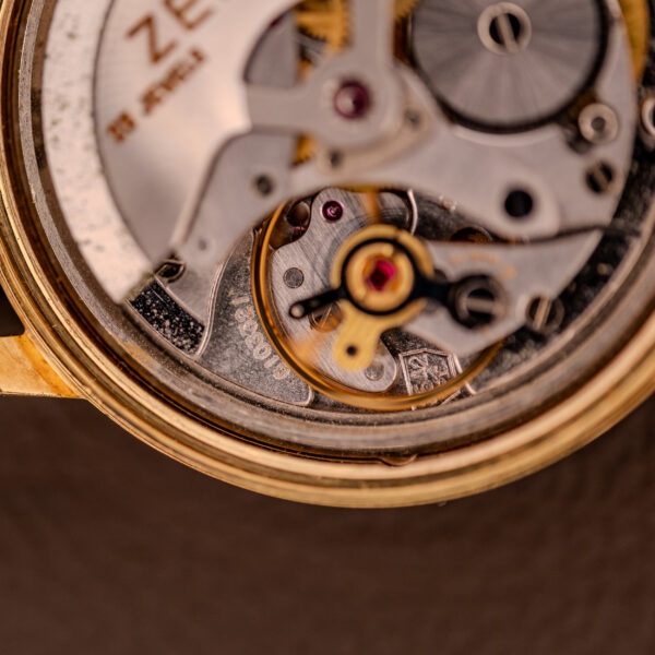 Close-up of the Zenith Automatic Date Cal. 2542, showcasing its intricate 25-jewel movement with gears, screws, and fine metal details beneath a striking sunburst dial.