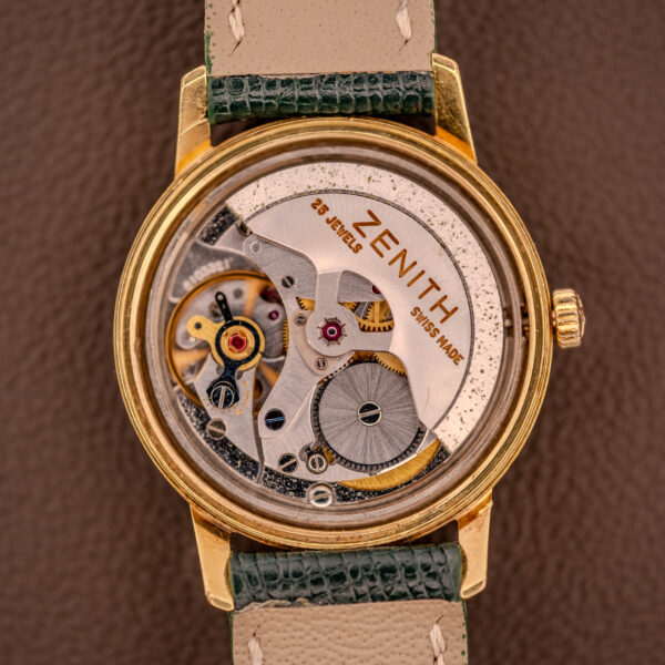 Zenith Automatic Date Cal. 2542 25 Jewels Sunburst Dial watch with visible mechanical movement, green leather strap, displayed on a brown background.