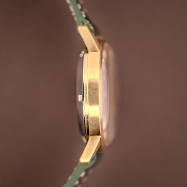 Side view of the Zenith Automatic Date Cal. 2542 25 Jewels with a sunburst dial and green strap, displayed against a brown background.