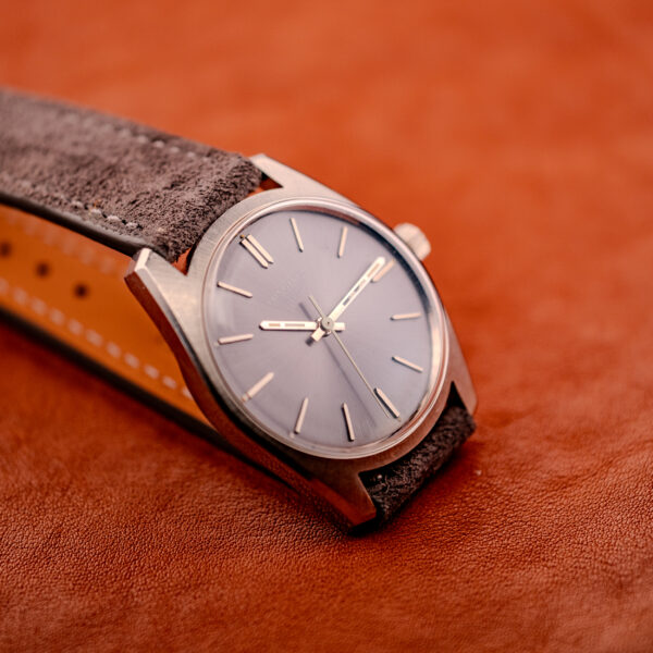 A Longines Admiral HF Anthracite Sunburst Dial Ref. 2301 Cal. 6942 c.1972 with a brown suede strap rests on a textured brown leather surface.