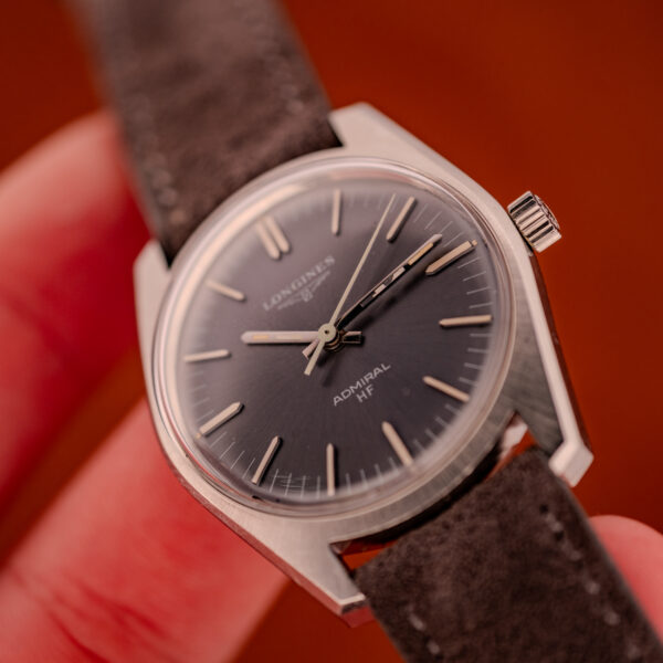 A close-up of a Longines Admiral HF Anthracite Sunburst Dial Ref. 2301 Cal. 6942 c.1972 wristwatch with a suede strap, held in hand.