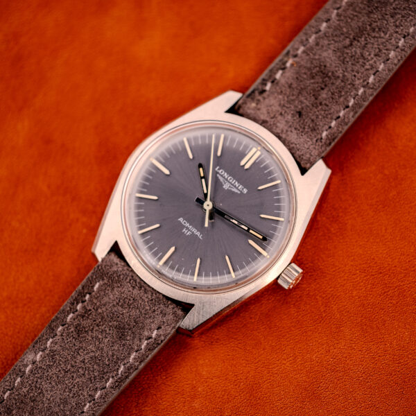A Longines Admiral HF Ref. 2301 Cal. 6942 c.1972 with an anthracite sunburst dial and suede strap rests on an orange leather surface.