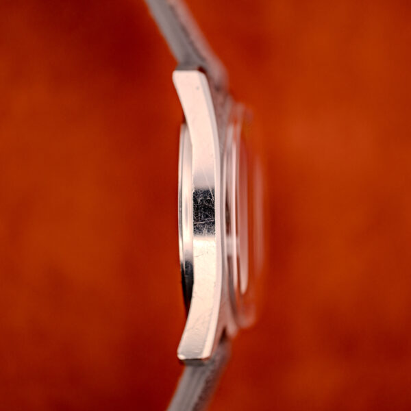 Side view of a Longines Admiral HF Anthracite Sunburst Dial Ref. 2301 wristwatch (c.1972) with Cal. 6942 movement, set against a blurred orange background.