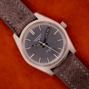 A Longines Admiral HF Ref. 2301 (c.1972) with an anthracite sunburst dial and suede strap, Cal. 6942, displayed against a vibrant orange background.