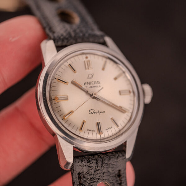 A hand holding an Enicar Sherpa Seapearl 600 Super Compressor Ref. 140/013 Cal. AR 1140 wristwatch with a black leather strap, silver dial, and the classic Super Compressor case.