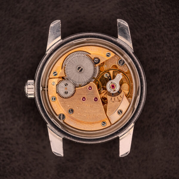 A close-up of the Enicar Sherpa Seapearl 600 Super Compressor Ref. 140/013 with Cal. AR 1140 movement shows visible gears and components, highlighting its Super Compressor design against a dark background.