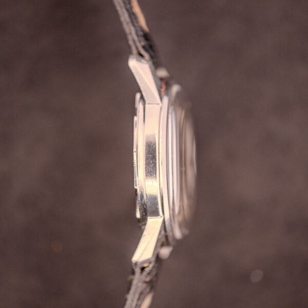A side view of an Enicar Sherpa Seapearl 600 Super Compressor Ref. 140/013 Cal. AR 1140 wristwatch with a leather strap is set against a blurred brown background.