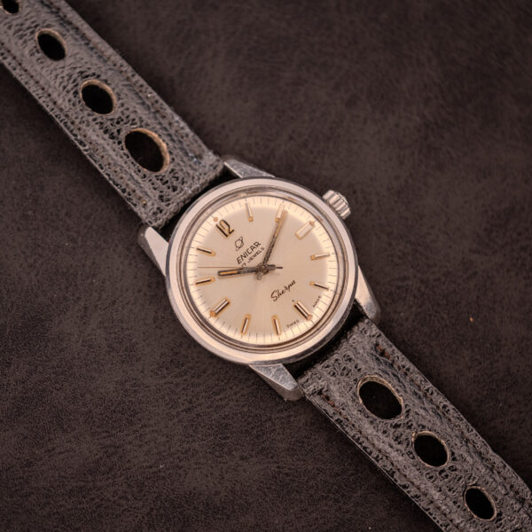 An Enicar Sherpa Seapearl 600 Super Compressor Ref. 140/013 Cal. AR 1140 wristwatch with a black perforated leather strap rests on a dark textured surface.