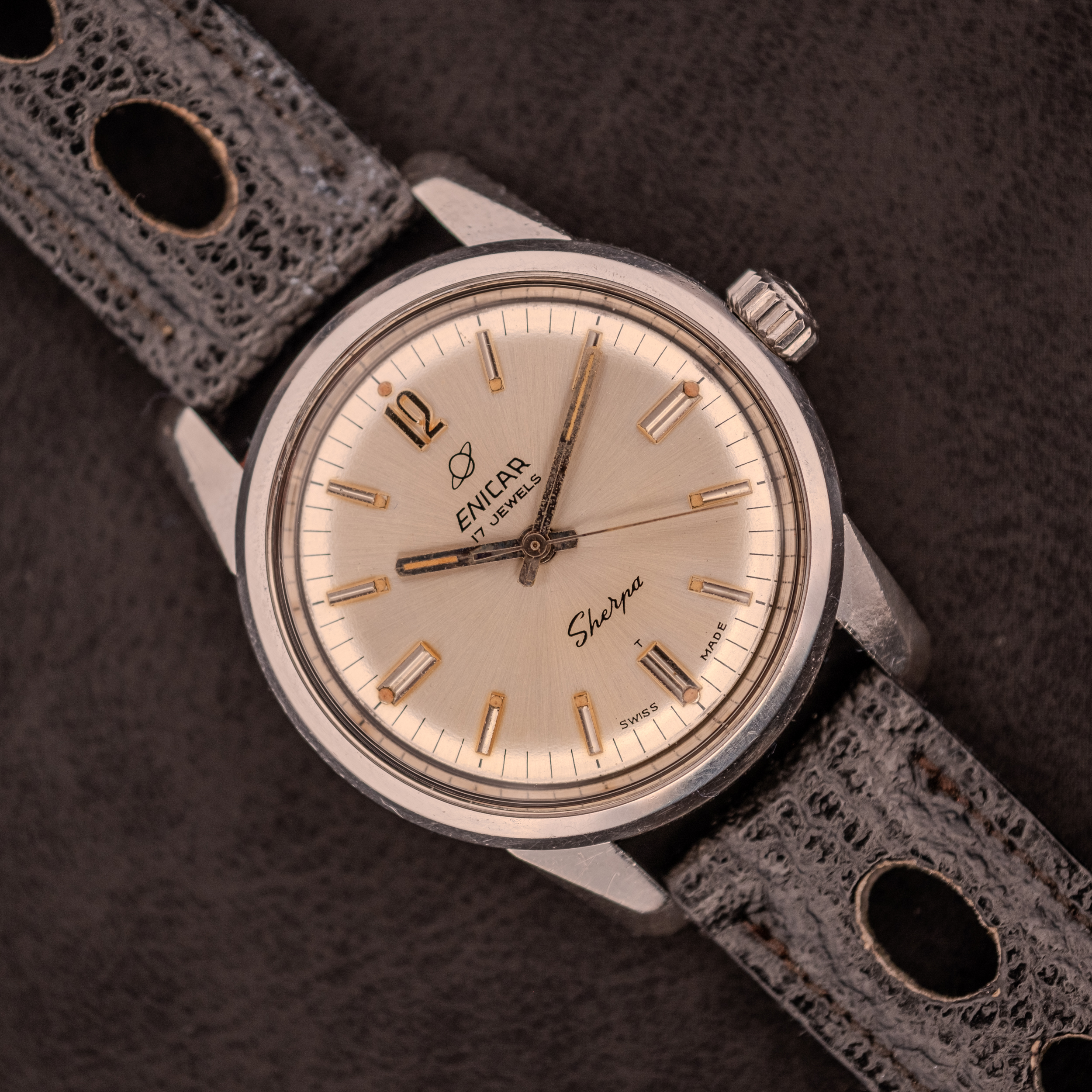 An Enicar Sherpa Seapearl 600 Super Compressor Ref. 140/013 Cal. AR 1140, featuring a beige dial and black perforated leather strap, highlights classic Super Compressor design on a dark surface. An Enicar Sherpa Seapearl 600 Super Compressor Ref. 140/013 Cal. AR 1140, featuring a beige dial and black perforated leather strap, highlights classic Super Compressor design on a dark surface.