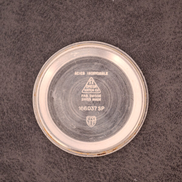 Round metal watch case back with Omega logo and engraved text, showing Omega Seamaster Automatic Date Ref. 166.037 Cal. 565 c.1968, on a dark textured surface.