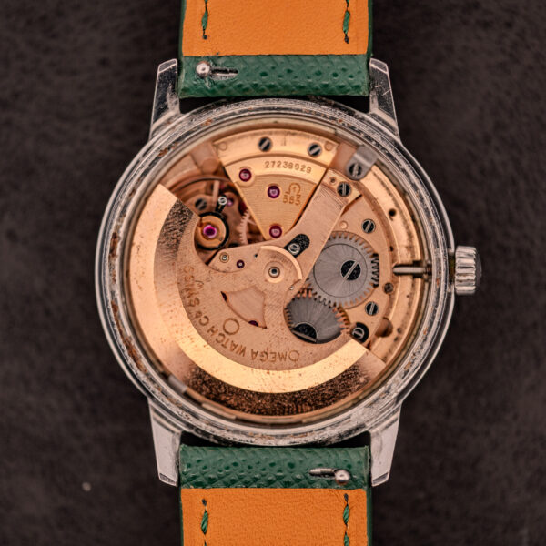 A close-up of the Omega Seamaster Automatic Date Ref. 166.037 Cal. 565 c.1968 highlights its intricate gears and signature green leather strap, featuring the Cal. 565 movement from circa 1968.