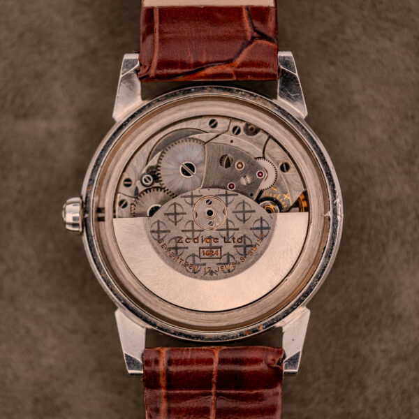 Back of a Zodiac Glorious Automatic "Faceted Bezel" Ref. 696 Cal. 1624 with visible gears, Zodiac Ltd. engraving, brown leather strap, on a textured surface.