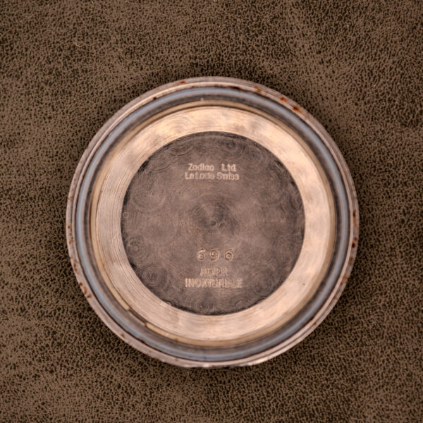 Round metal caseback on a textured brown surface, engraved with Zodiac Ltd Le Locle Swiss, Cal. 1624—a refined detail from the Zodiac Glorious Automatic "Faceted Bezel" Ref. 696 Cal. 1624.