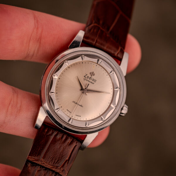 A hand holding the Zodiac Glorious Automatic "Faceted Bezel" Ref. 696 Cal. 1624 watch with a brown leather strap and silver dial.