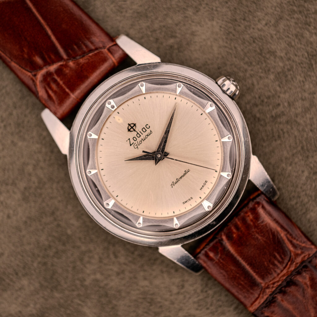 A Zodiac Glorious Automatic "Faceted Bezel" Ref. 696 Cal. 1624 wristwatch with a brown leather strap and silver dial rests elegantly on a textured surface.