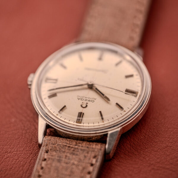 Close-up of an Omega Seamaster Automatic "Red Crosshair" Ref. 165.002 Cal. 552 with a beige dial, subtle red crosshair, and brown leather strap, shown resting on a bold red surface.