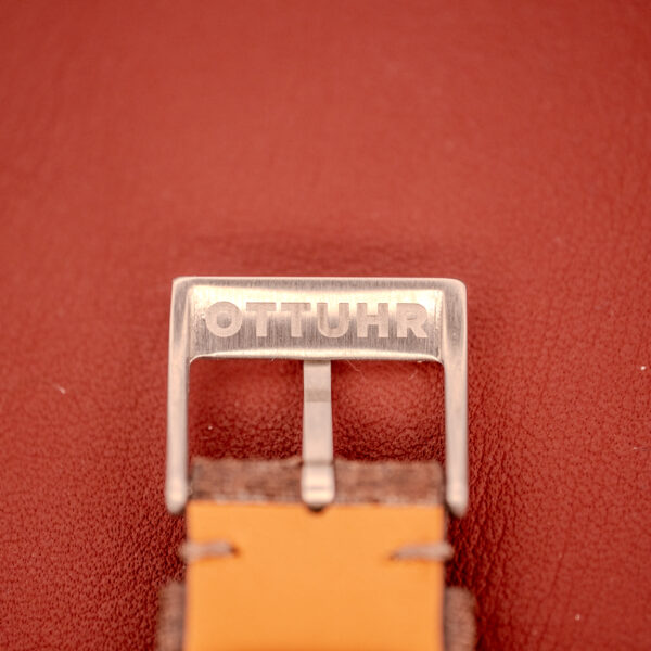 A silver OTTUHR-engraved buckle secures a brown leather strap, set against a red background inspired by the Omega Seamaster Automatic "Red Crosshair" Ref. 165.002 Cal. 552.