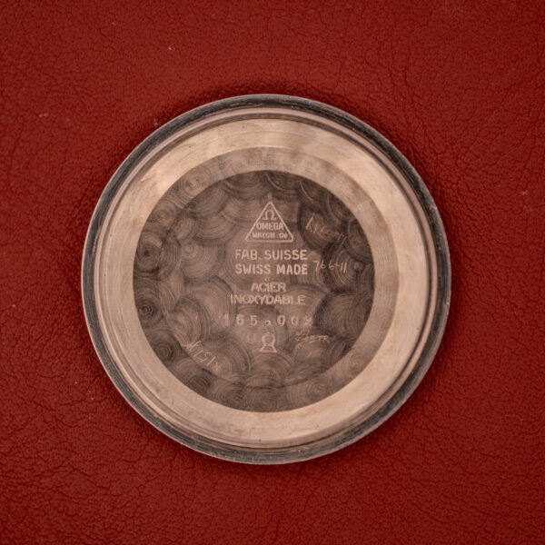 The Omega Seamaster Automatic "Red Crosshair" Ref. 165.002 Cal. 552, with an engraved stainless steel back, is shown on a red textured background.