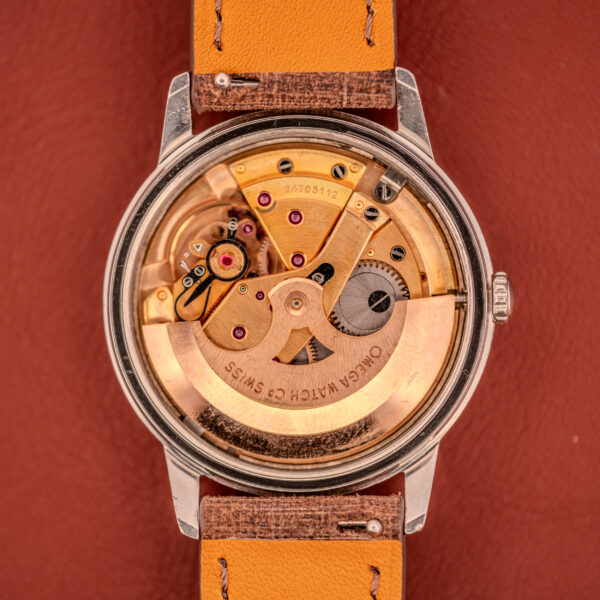 Close-up of the Omega Seamaster Automatic "Red Crosshair" Ref. 165.002 Cal. 552’s exposed movement with a tan leather strap, resting on a brown surface.