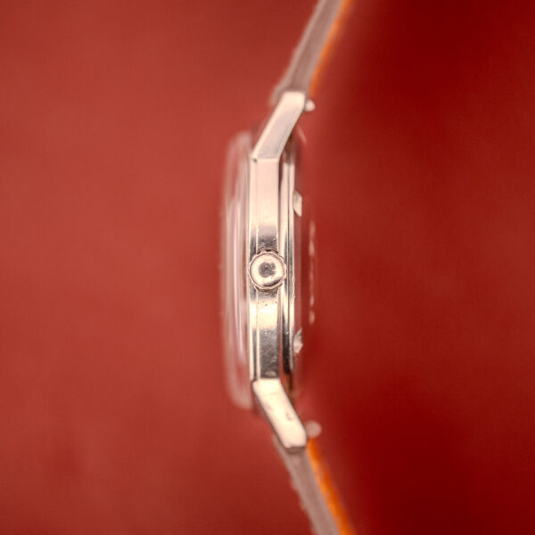 Side view of an Omega Seamaster Automatic "Red Crosshair" Ref. 165.002 wristwatch with Cal. 552 movement and a leather strap, set against a reddish-brown background.