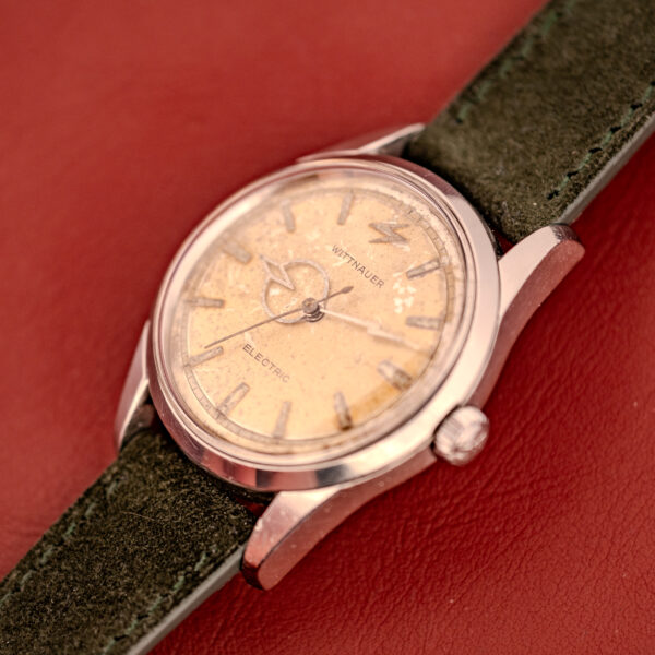 A Wittnauer Electro-Chron "Lightning Bolt" Tropic Dial Ref. 6150 with a green strap sits on a red leather surface.