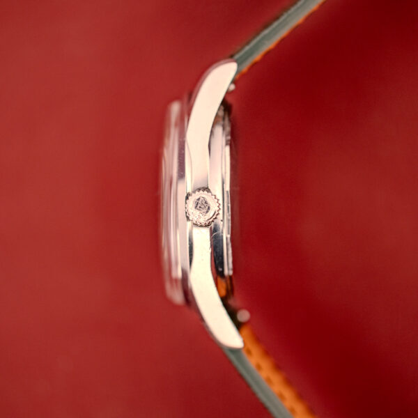 Side view of a Wittnauer Electro-Chron "Lightning Bolt" Tropic Dial Ref. 6150 silver wristwatch with a brown leather strap set against a red background.