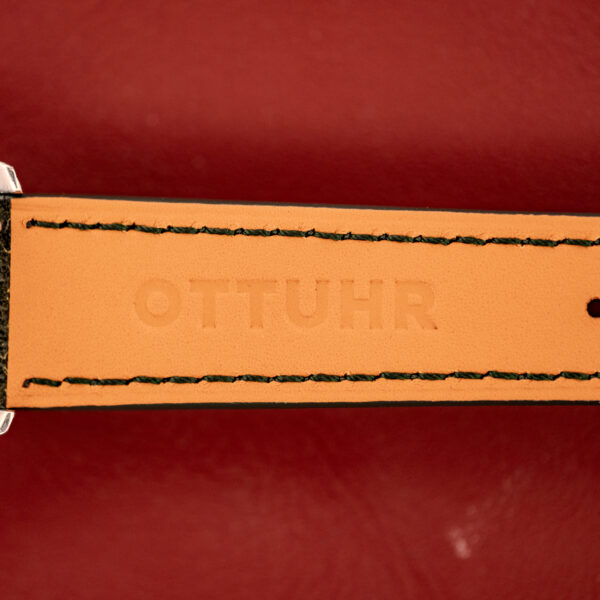 Close-up of a tan leather watch strap embossed with OTTUHR, set against a red background—ideal for pairing with your Wittnauer Electro-Chron "Lightning Bolt" Tropic Dial Ref. 6150 or any watch with a bold tropic dial.