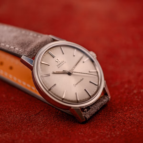 Beauty shot of Omega Seamaster 165.002 silver sunburst dial in three-quarter view on grey suede strap and red velvet