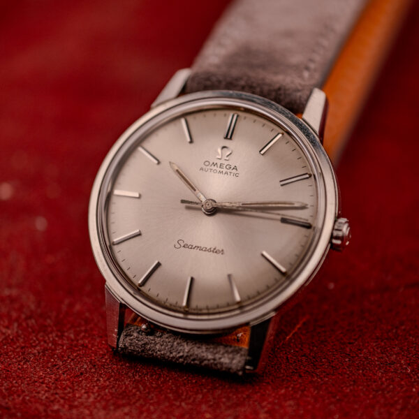 An Omega Seamaster Automatic Ref. 165.002 with Cal. 552 movement and a brown leather strap rests on a red textured surface.