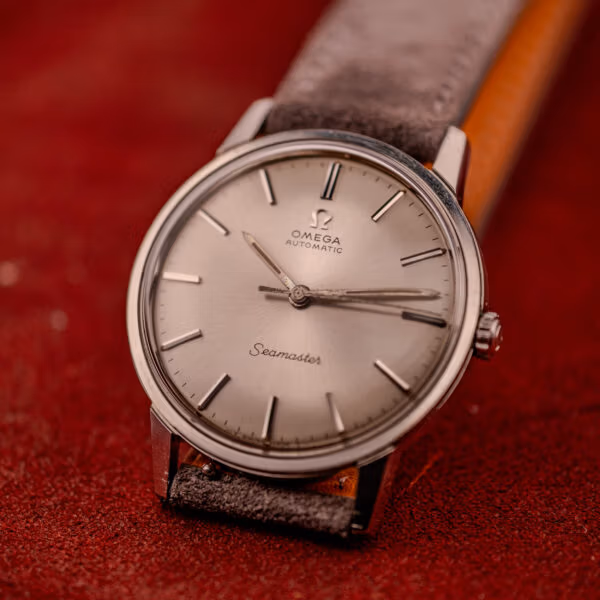 Omega Seamaster 165.002 face-up on grey suede strap with the full silver sunburst dial and applied stick markers visible
