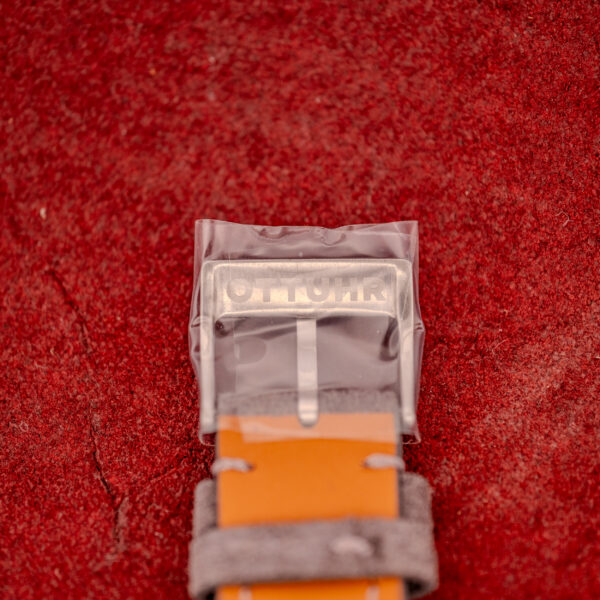 A silver OTTOUR buckle on a tan leather strap, paired with an Omega Seamaster Automatic Ref. 165.002 Cal. 552, rests elegantly on a textured red surface.