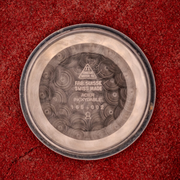 Omega Seamaster Automatic Ref. 165.002 Cal. 552 round silver case back with engraved text, displayed on a textured red surface.