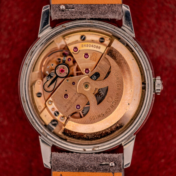 Close-up of an Omega Seamaster Automatic Ref. 165.002 Cal. 552 movement, highlighting intricate gears and engraved Cal. 552 markings set against a vivid red background.