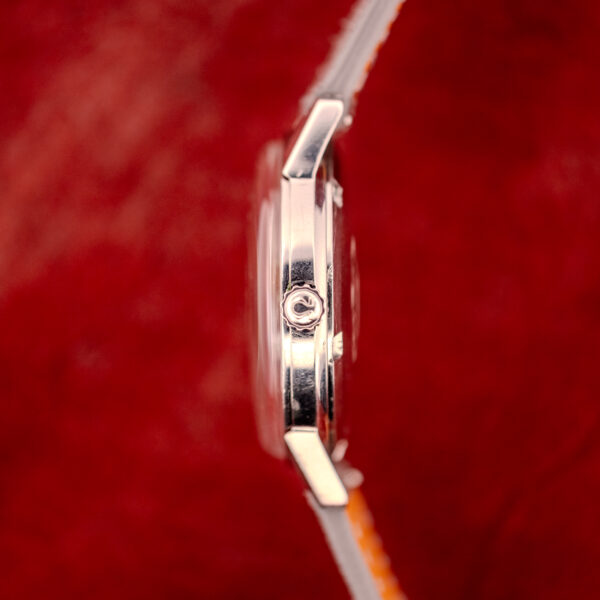 Side view of an Omega Seamaster Automatic Ref. 165.002 Cal. 552 with a silver case and vibrant orange strap, set against a blurred red background.