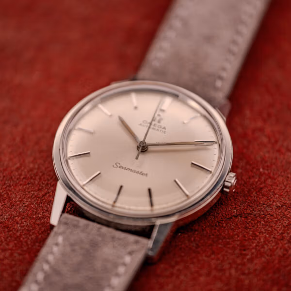 Three-quarter angle of Omega Seamaster ref. 165.002 silver sunburst dial showing slim case profile and grey suede strap