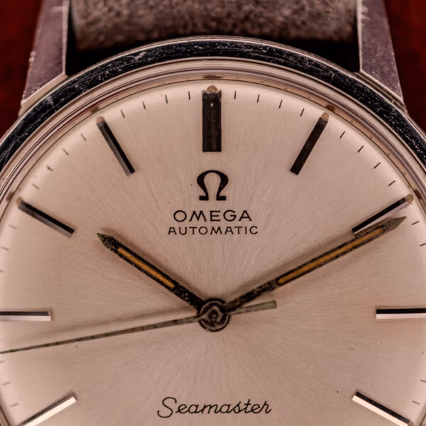 Macro close-up of Omega Seamaster 165.002 dial showing Omega logo applied stick markers and aged sword hands