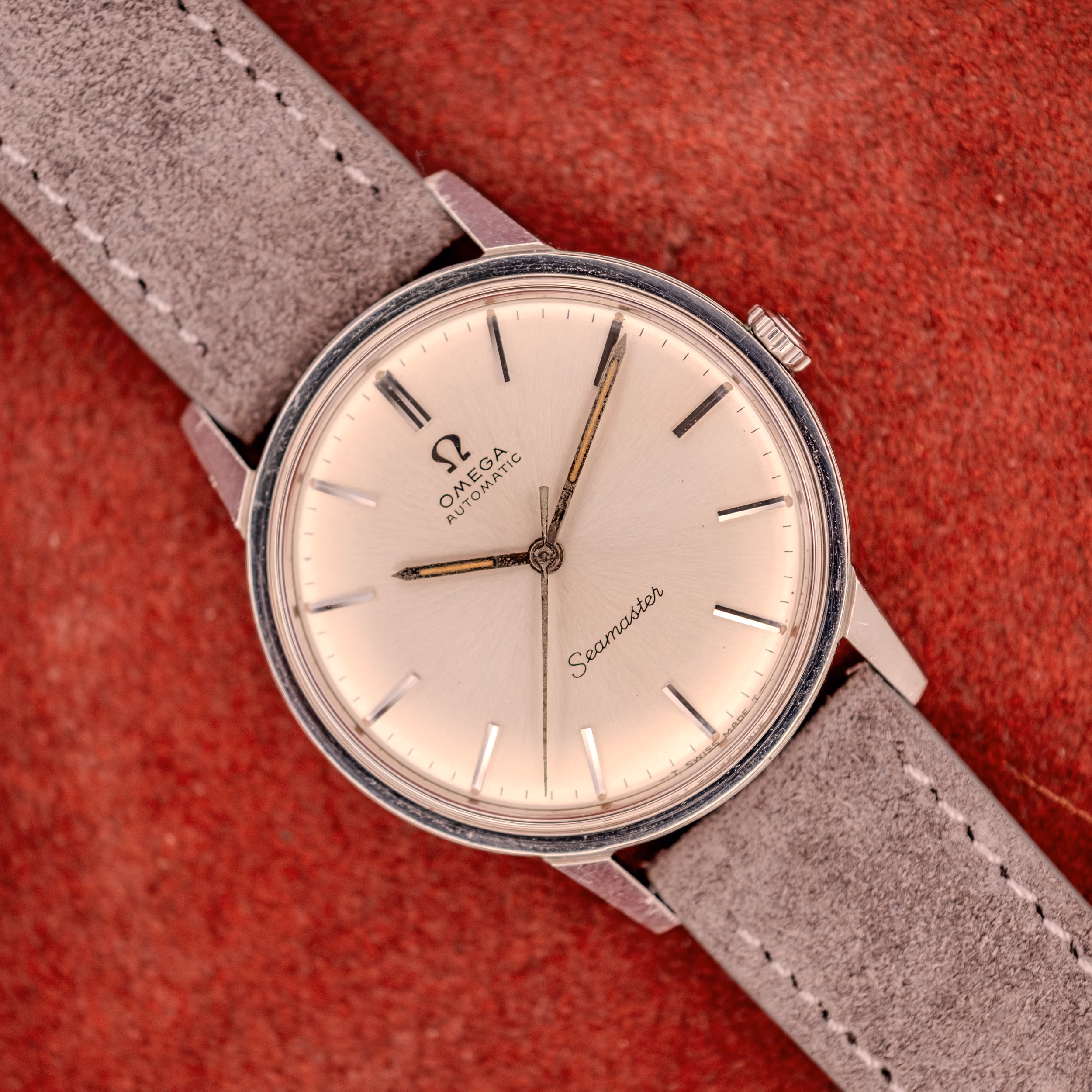 Omega Seamaster 165.002 silver sunburst dial straight-on on grey suede strap and red velvet backdrop