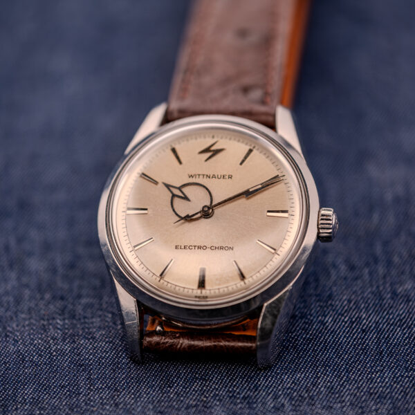 A Wittnauer Electro-Chron "Lightning Bolt" Ref. 6150/2 Cal. 11EW c.1962, featuring a brown leather strap and striking Lightning Bolt seconds hand, is displayed on blue denim fabric.