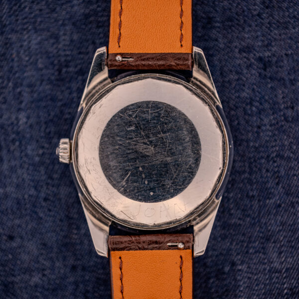 The Wittnauer Electro-Chron "Lightning Bolt" Ref. 6150/2 Cal. 11EW c.1962, featuring a brown leather strap, rests on denim. The scratched caseback is engraved with the name JOHN.