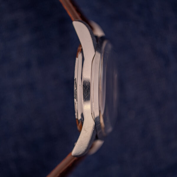 Side view of a Wittnauer Electro-Chron "Lightning Bolt" Ref. 6150/2 Cal. 11EW c.1962 silver wristwatch with a brown leather strap, set against a dark blue textured background.
