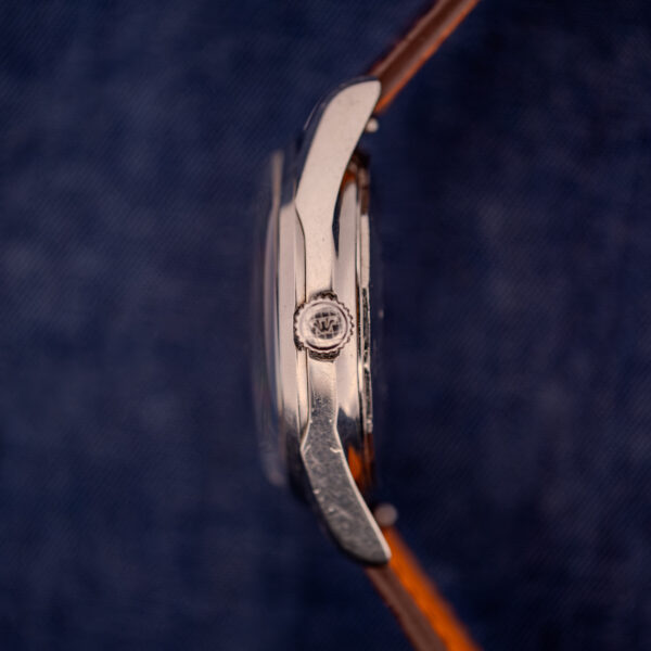 Side view of a Wittnauer Electro-Chron "Lightning Bolt" Ref. 6150/2 Cal. 11EW c.1962 with a brown leather strap, shown against a blue textured background.