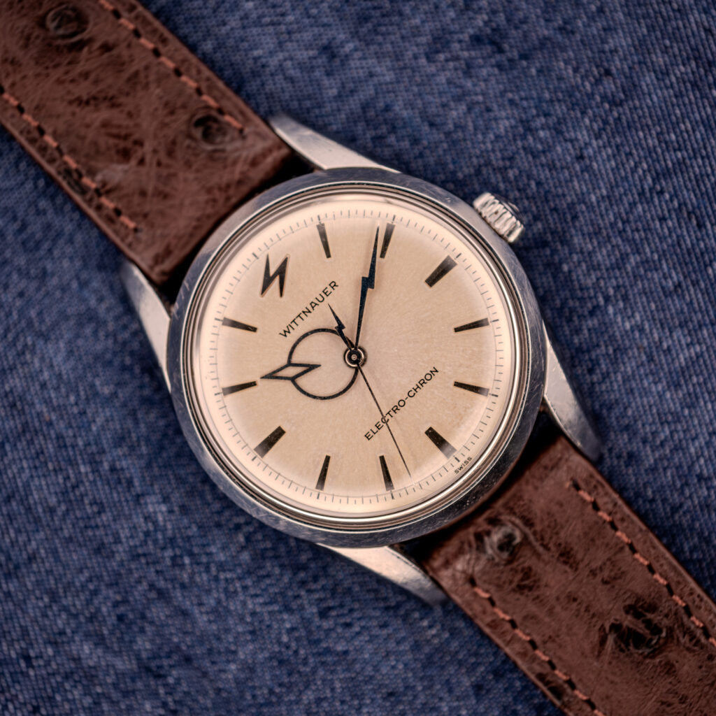 A Wittnauer Electro-Chron "Lightning Bolt" Ref. 6150/2 Cal. 11EW c.1962 with a brown leather strap, shown on blue fabric, highlights the timeless appeal of this iconic vintage wristwatch design.