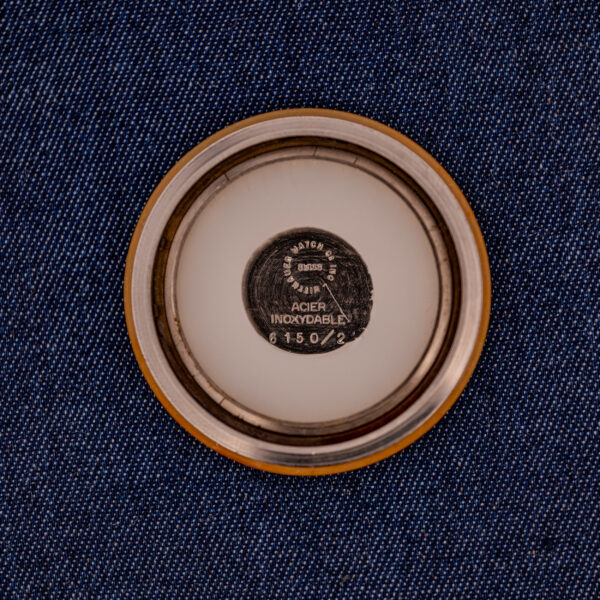 A round metal case back engraved "Ref. 6150/2" from a Wittnauer Electro-Chron "Lightning Bolt" Cal. 11EW c.1962 rests on blue denim fabric.