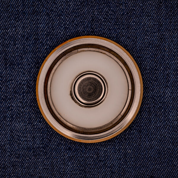 A close-up of a round metal button on dark blue denim echoes the sleek style of the Wittnauer Electro-Chron "Lightning Bolt" Ref. 6150/2 Cal. 11EW c.1962, highlighted by its subtle lightning bolt motif.