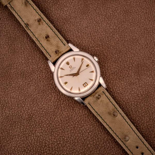 An Omega Transitional Calendar Bumper Automatic Ref. 2438-2 Cal. 353 c.1951 wristwatch with a tan leather strap displayed on a textured brown surface.