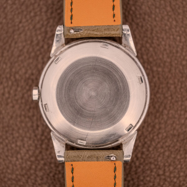 A close-up of the back of an Omega Transitional Calendar Bumper Automatic Ref. 2438-2 Cal. 353 c.1951 with a tan leather strap, highlighting its refined design on a brown textured surface.